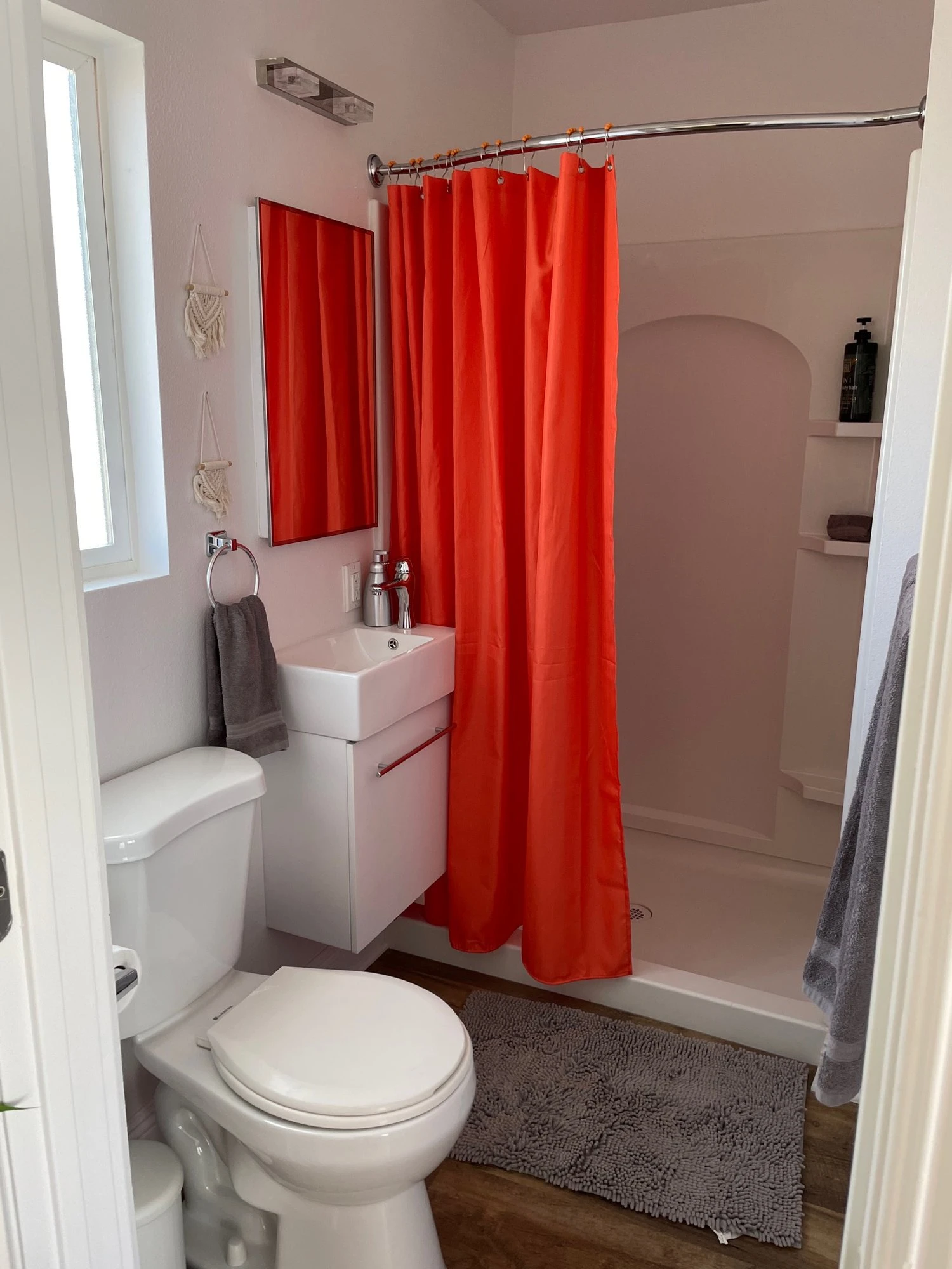 An orange-red shower curtain adds a pop of color to an otherwise white bathroom at The Tree Ten Hotel in Palm Springs, California