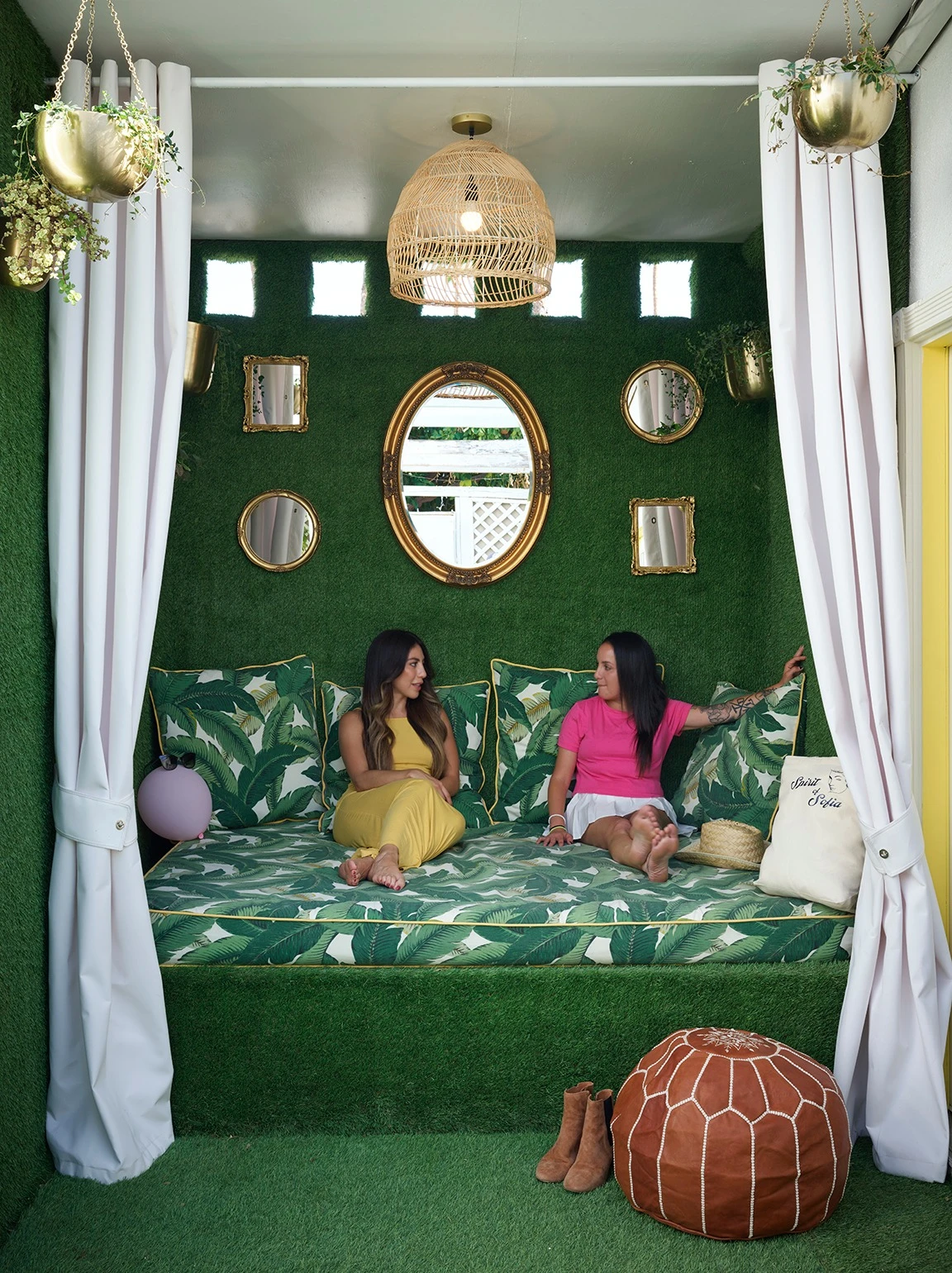 Two women sit next to each other on a green day bed outside at the Spirit of Sofia boutique hotel in Palm Springs, California