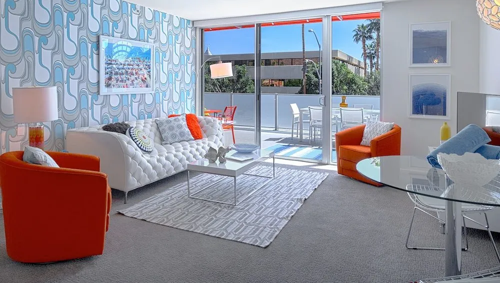 A room at The Twist Palm Springs hotel decorated in a mid-century modern style with a red chair and puffy couch
