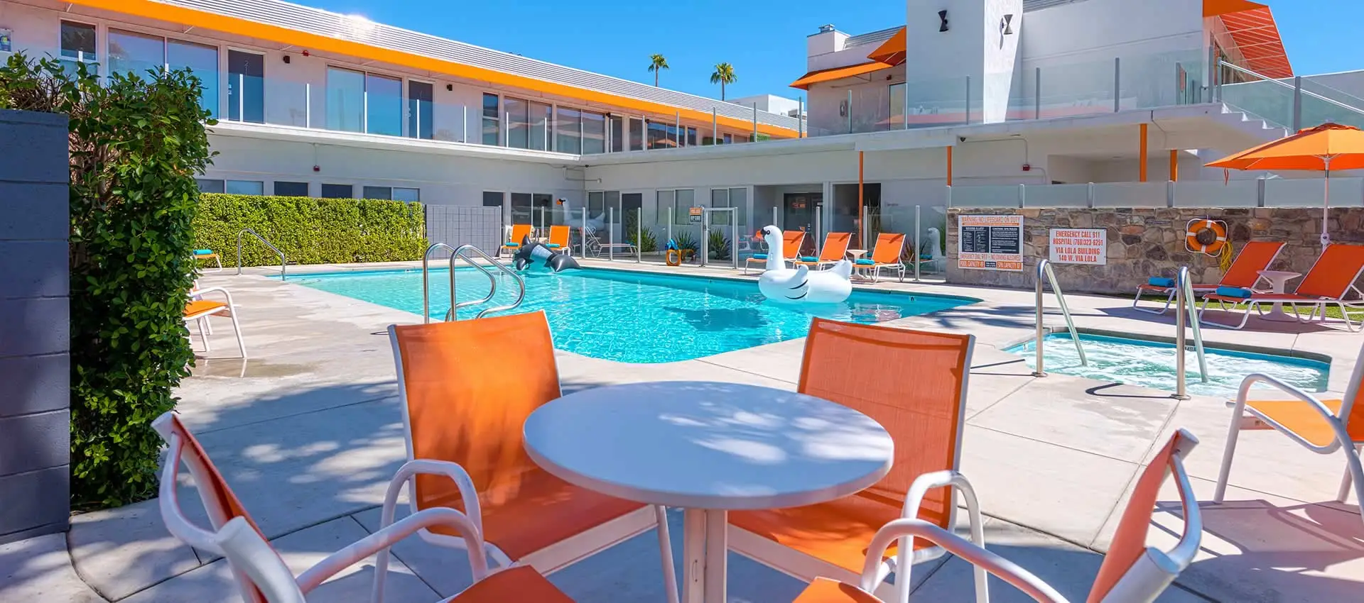 A white table and orange chairs next to the pool at The Twist Palm Springs