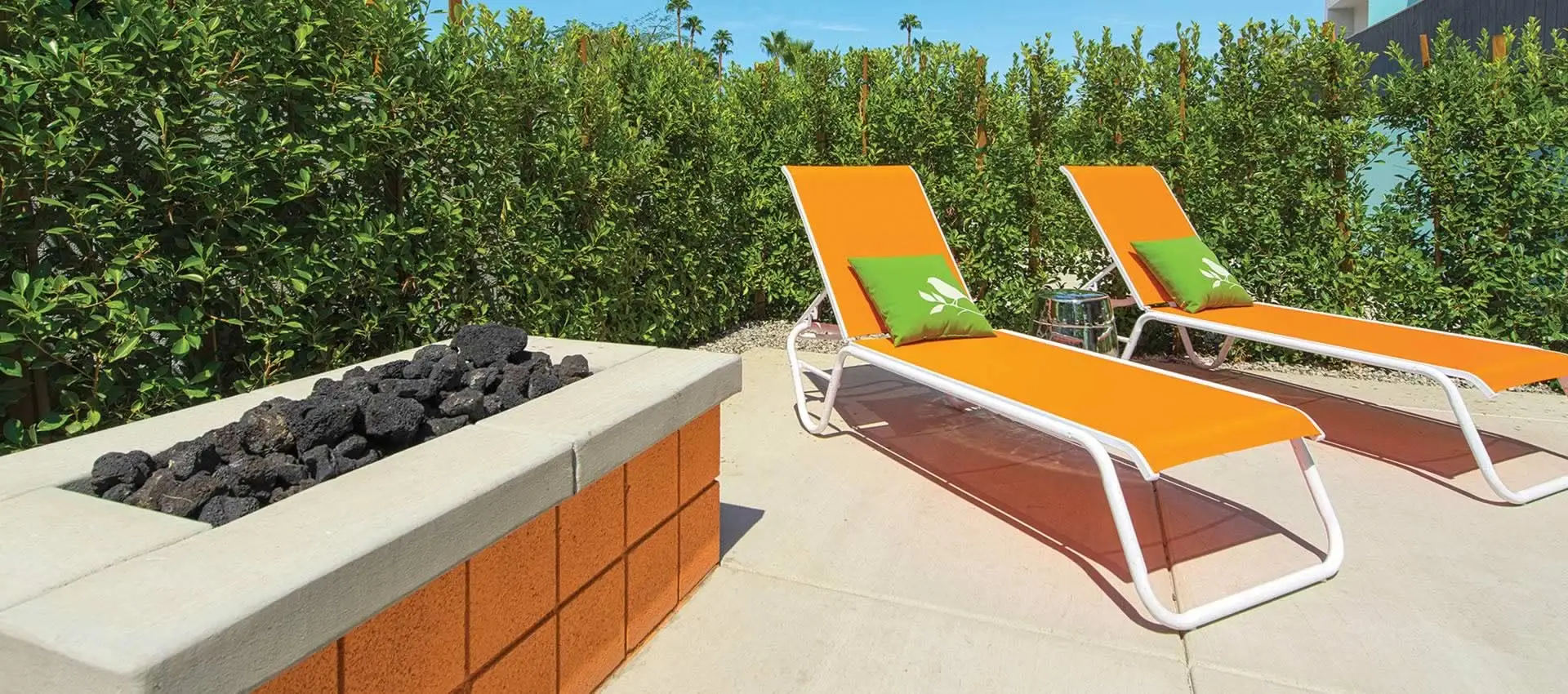 Two orange lounge chairs with green pillows on them next to a fire pit at The Twist Palm Springs boutique hotel