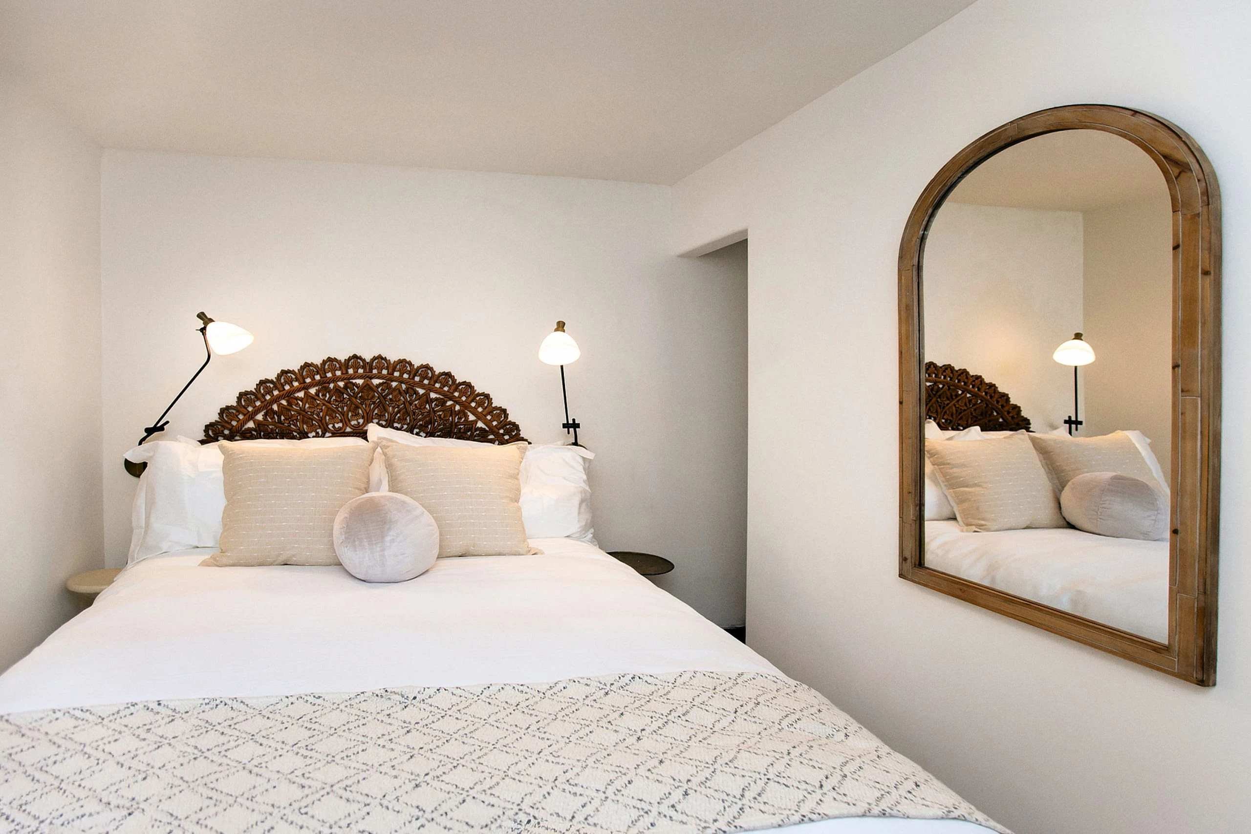 The inside of a room at The Lucille Palm Springs with a wooden headboard and white comforter covering the bed and a mirror on the wall
