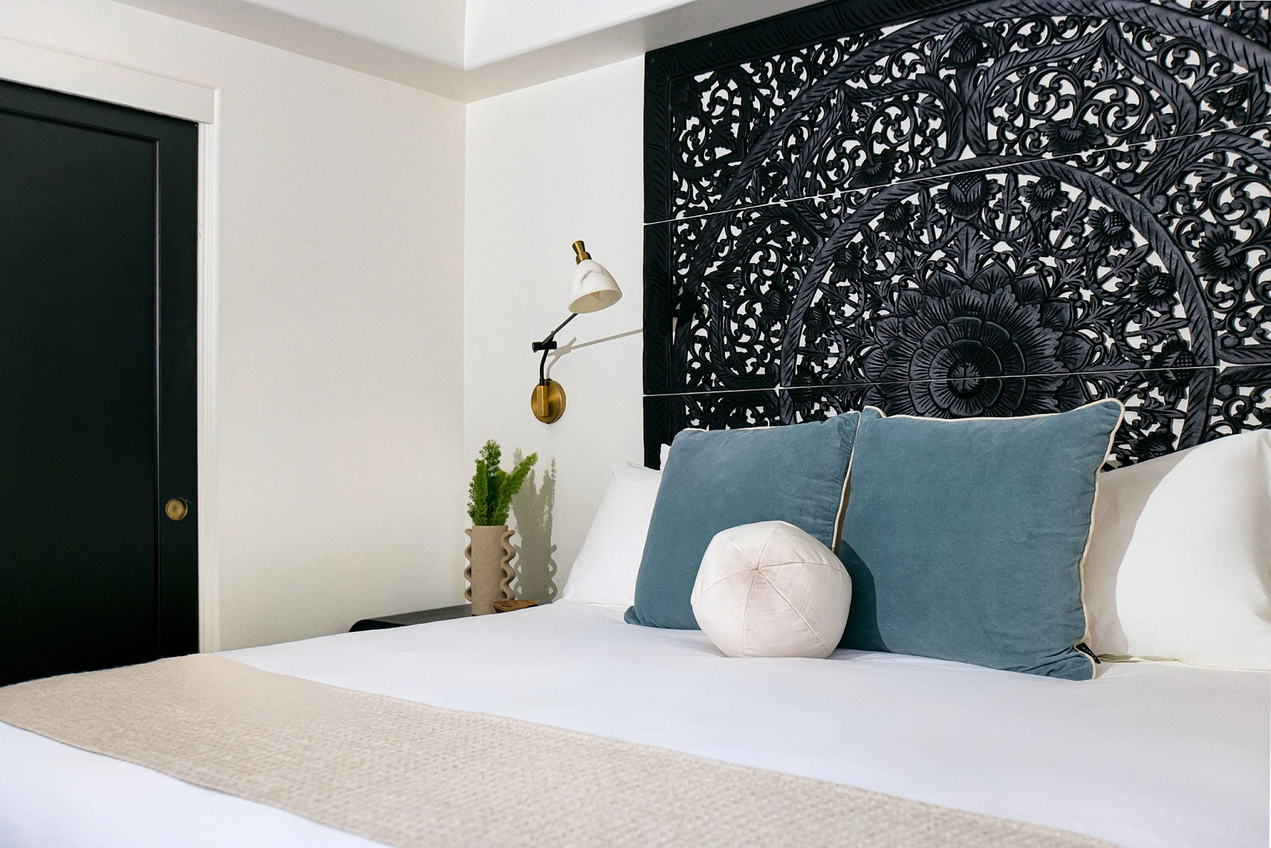 A bed at The Lucille Palm Springs with blue pillows on it and a beige blanket and white comforter
