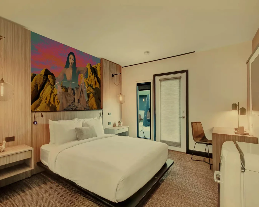 A room at Mahala Hotel in Palm Springs, California, with a large art print of Cher on the wall above a bed with white linens