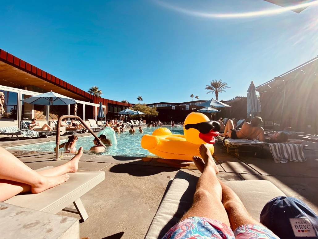 A man relaxes on a chaise lounge by the pool in Palm Springs, California, with a rubber duck float in the water