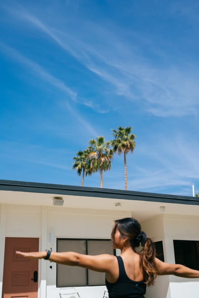 A woman with long dark hair practices yoga outside on a sunny day at the Azure Aky Resort in Palm Springs, California