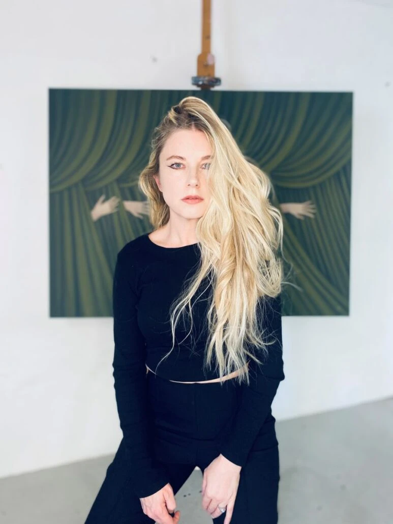 A blonde woman sits in front of a painting