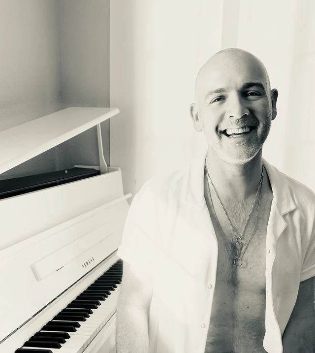 A black and white photo of a smiling bald man sitting at a piano