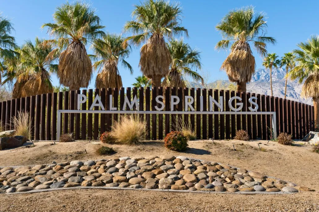 A silver metal Palm Springs sign in front of a wooden fence
