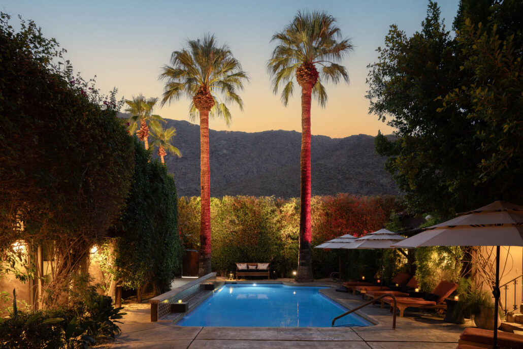 A pool surrounded by palm trees at Talavera Palm Springs at sunset
